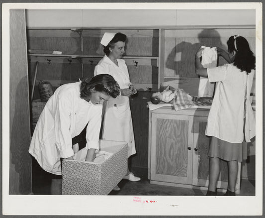 Eleven Mile Corner, AZ. FSA farm workers' community. Girls, who live at the NYA resident center learning baby care. The nurse, who divides her time between working at the hospital and instructing the NYA girls, is showing them how to care for a well baby
