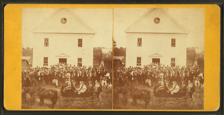 Crowd in front of two story building including women in a carriage and a band.