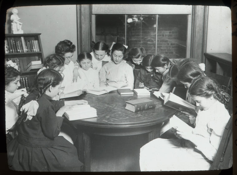 Tremont, interior view, girls gathered around table reading under guidance of "Miss Farren(?)"  "...ford Club,"