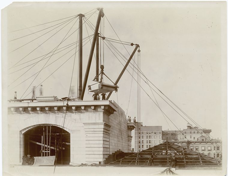 Exterior marble work : construction workers lowering a piece of marble into place on the roof, looking north