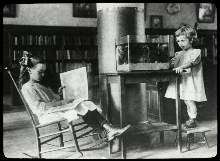 Riverside, girl reads as another smaller girl looks at aquarium