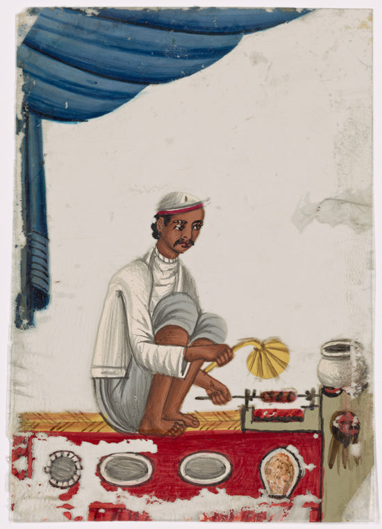 Seated male food vendor roasting meat on spit,  fanning flames