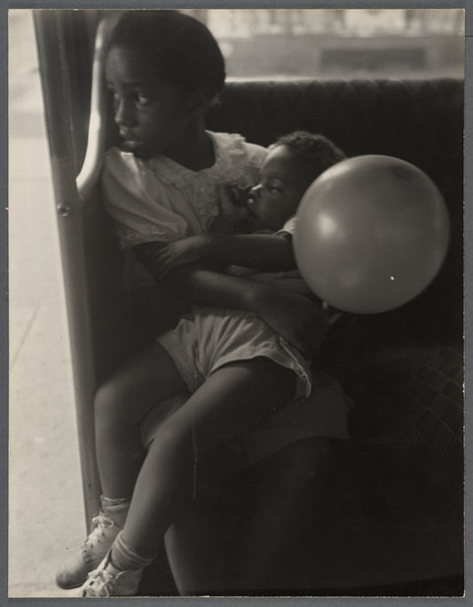 Young girl holds a toddler in her lap, and a balloon in hand