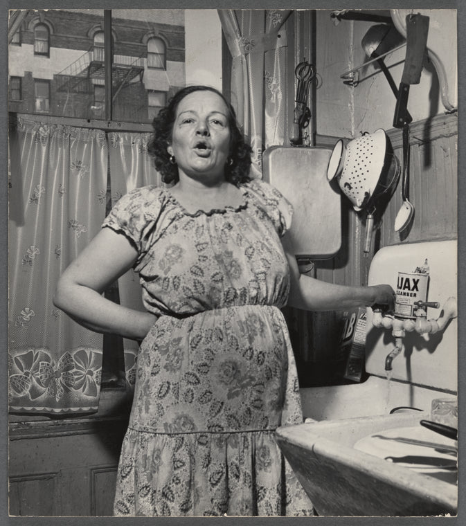 A woman with a stained dress stands in an apartment kitchen