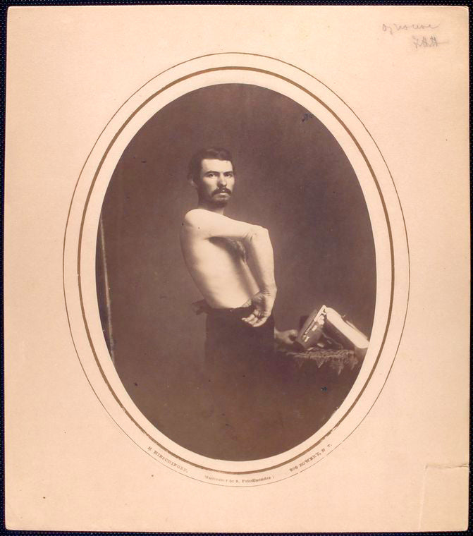 [Shirtless man stands sideways displaying right forearm, brace lies on tabletop] / H. Hirschinger