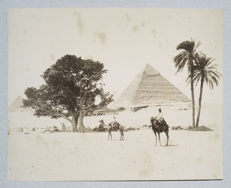 Two men riding camels in front of a pyramid