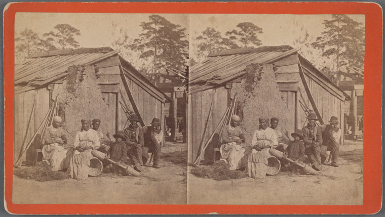Family group sitting in front of a wooden shack.