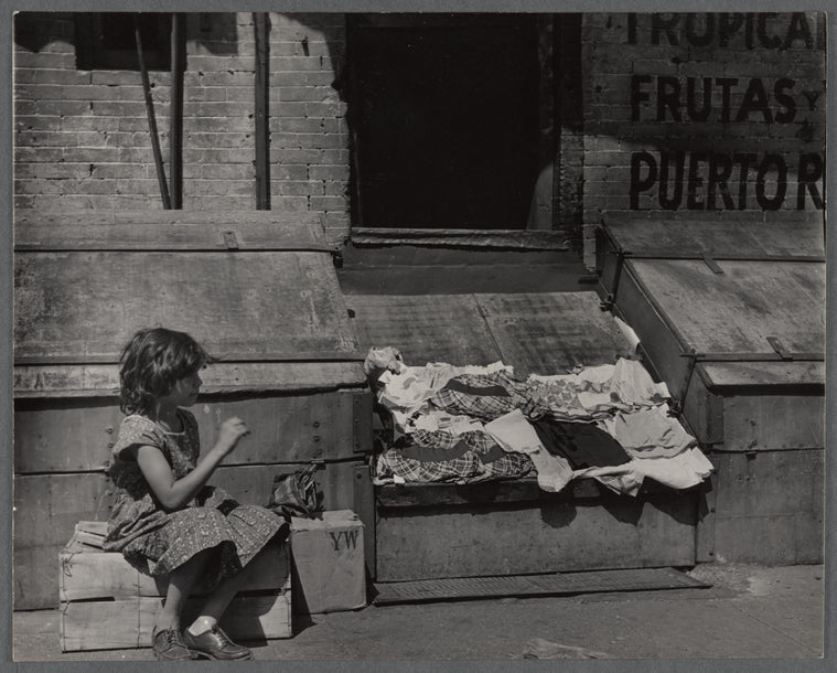 Young girl seated on a cardboard box on street sidewalk
