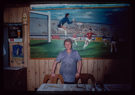 Restaurant worker in blue shirt in front of painting, Nea Hellas