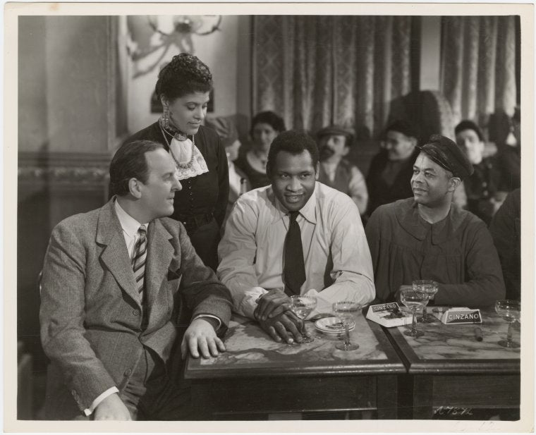 Eslanda Goode Robeson (standing), Paul Robeson (center), and Lawrence Brown (right) in a scene from the motion picture "Big Fella"