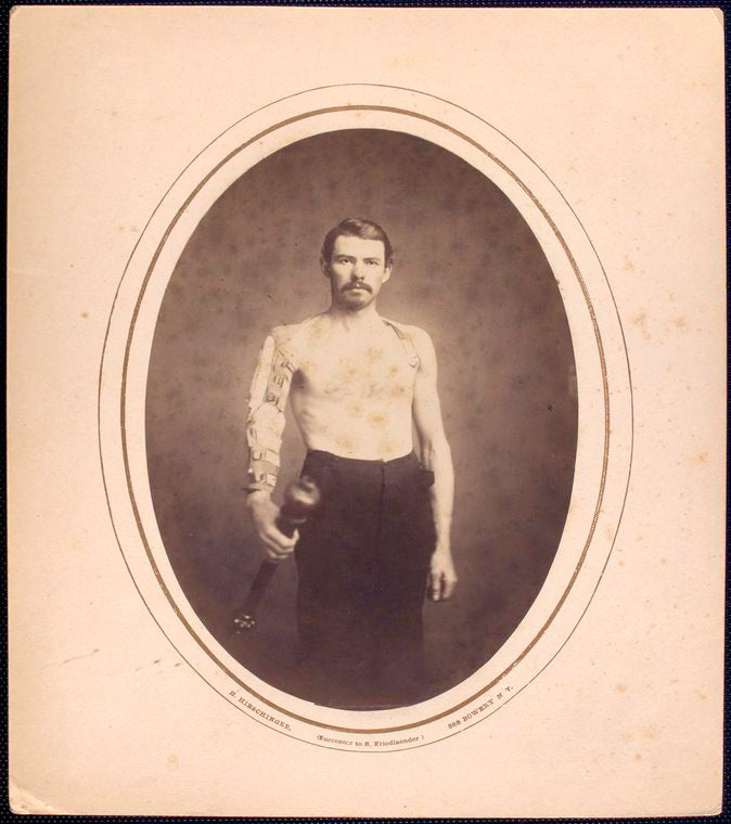 [Shirtless man stands with right arm in brace and harness, grasps long wooden pole in hand] / H. Hirschinger