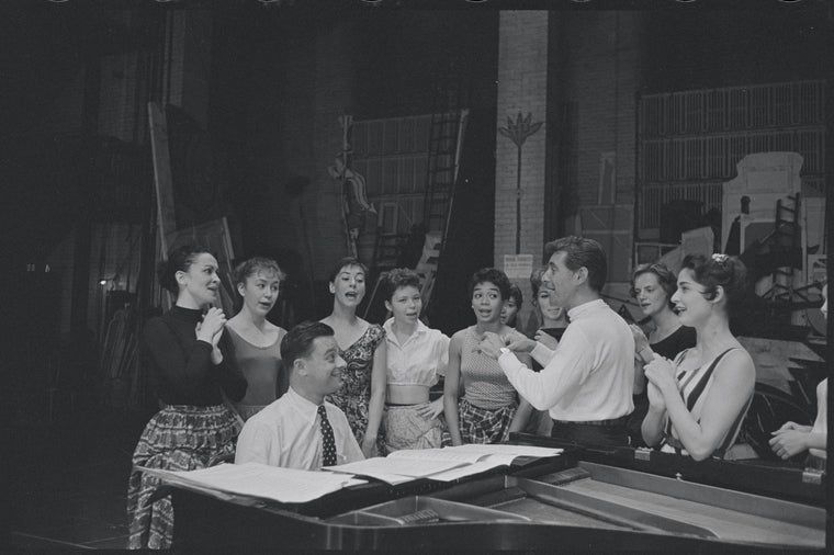 Chita Rivera, Stephen Sondheim, Leonard Bernstein, Carol Lawrence, and cast around piano in rehearsal for the stage production West Side Story