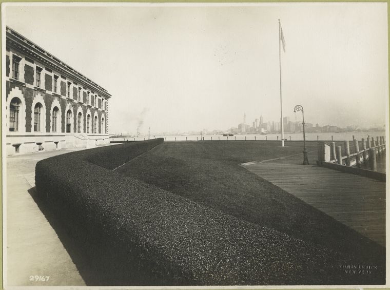 View of one wing of the Immigration Station, Ellis Island, showing New York skyline in the distance.