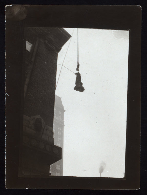 Harry Houdini suspended upside down in a bag from a building roof