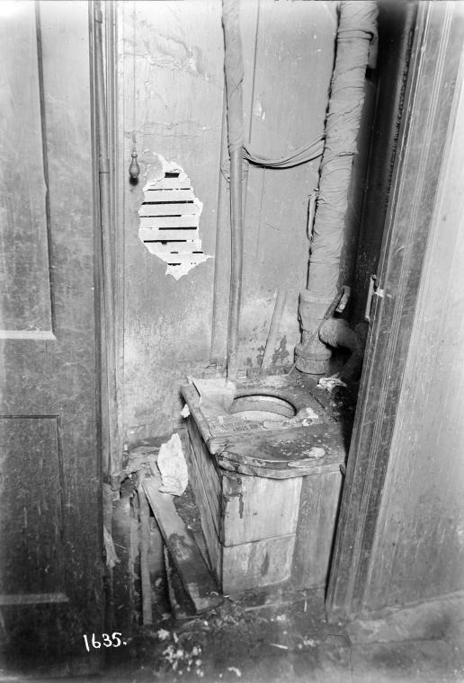 Toilet with newspaper on seat and pipes bound in rags