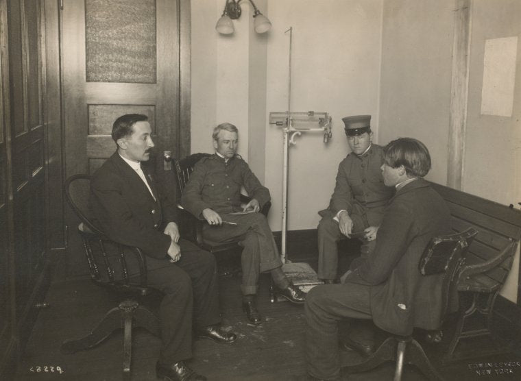 A private interview between a young immigrant and an Ellis Island official. Two staff members [?] are also present