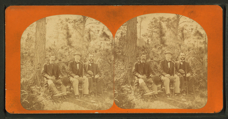 Three gentlemen pose on rustic bench, each holding a walking stick.