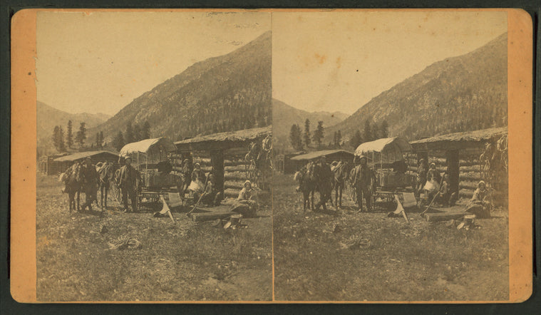 Group in front of a log cabin with a covered wagon.