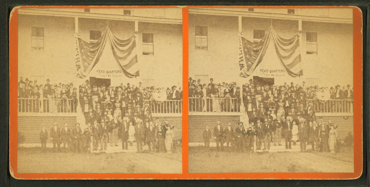 Group of men and women posing on steps of large building, flag draped overhead, and a sign reading "Headquarters First ME Cavalry".