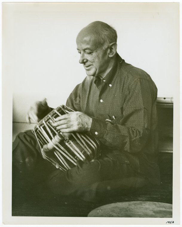 Henry Cowell trying out one of the five tablas for the tablatarang (= circle of tuned drums) presented to him for his Symphony No. 13 (Madras) by the Music Academy of Madras, India.  NYC, 1959