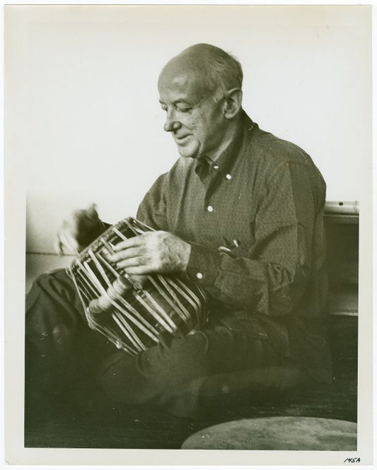 Henry Cowell trying out one of the five tablas for the tablatarang (= circle of tuned drums) presented to him for his Symphony No. 13 (Madras) by the Music Academy of Madras, India.  NYC, 1959