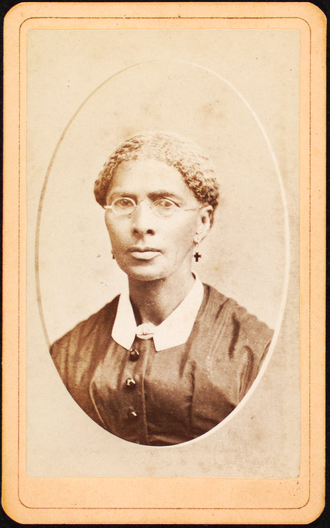 Studio portrait of woman wearing glasses and cross-shaped earrings.